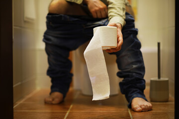 Man Holding Toilet Paper Roll Sitting on Toilet in Bathroom - Hygiene, Daily Routine Concept
