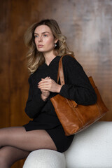 A girl in a warm sweater, a black short skirt, nylon tights, and black shoes is posing with a brown...
