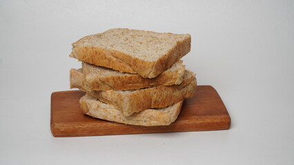 A stack of whole wheat bread served on a brown wooden board placed on a white background (isolated white).
