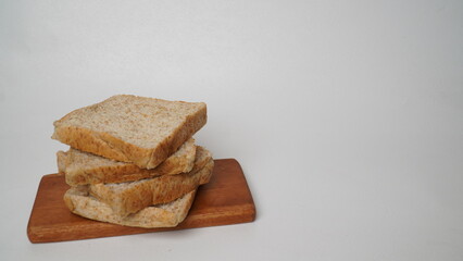 A stack of whole wheat bread served on a brown wooden board placed on a white background (isolated white).