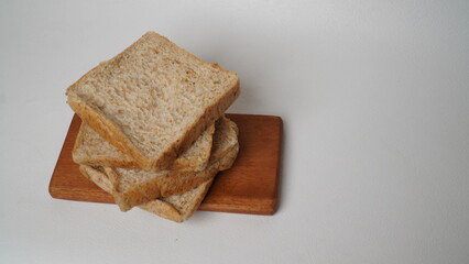 A stack of whole wheat bread served on a brown wooden board placed on a white background (isolated white).