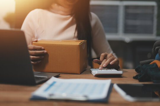 Startup SME small business entrepreneur of freelance Asian woman wearing apron using laptop and box to receive and review orders online to prepare to pack sell to customers, online sme business ideas.