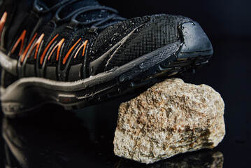 Close-up of waterproof black hiking shoe with orange details on small rock. Rugged trekking boot on...