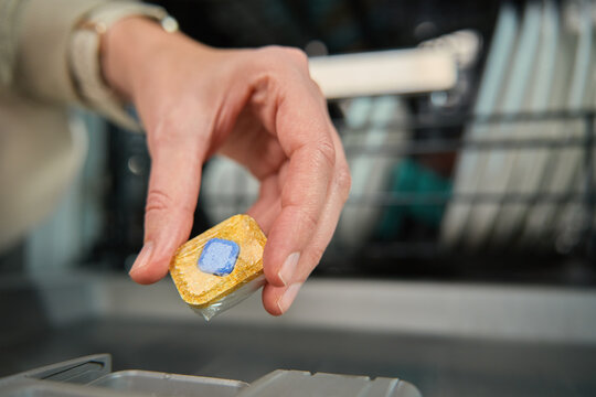 Close-up of female hand placing dishwasher detergent tablet into dispenser compartment. Efficient and hygienic dishwashing
