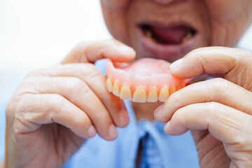 Asian senior woman patient holding teeth denture in her hand for chew food.