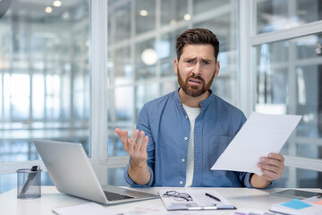 Fototapeta premium Portrait of a disappointed financier inside the office at the workplace, the man holds reports in his hands and looks sadly at the camera. Businessman dissatisfied with the results, bankruptcy.