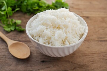 Cooked white rice or steamed rice in a white bowl with wooden spoon on wooden background