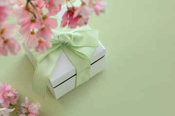 white gift box with green bow on green background and pink cherry blossoms.