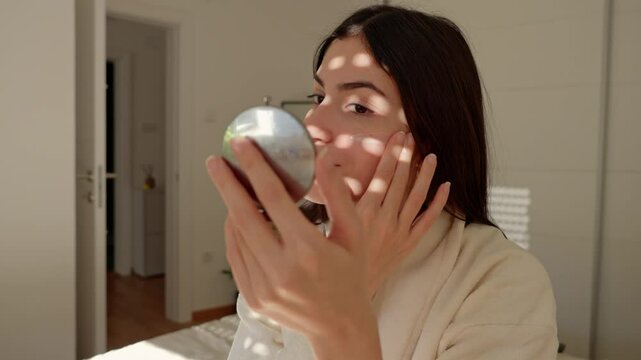 A woman smiling while applying facial cream to her skin, wearing a bathrobe and enjoying her skincare ritual. 4k video