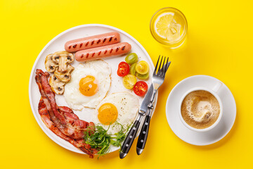 A classic breakfast plate featuring sunny-side-up eggs, crispy bacon, sausages, and fresh tomatoes
