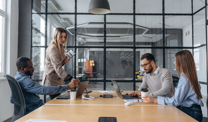 Calm, sitting by the table. Professional workers are in the modern office together