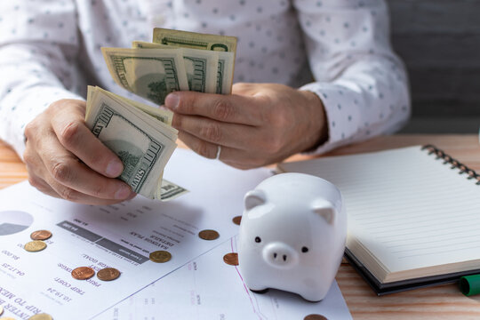 Saver counting dollar bills among papers, coins and piggy bank.
