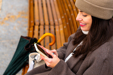 A woman sitting on a park bench, looking at her phone with a smile, scrolling through content