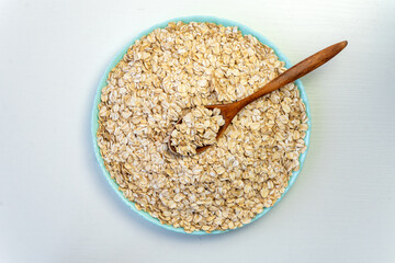 Dry oatmeal in a wooden plate and spoon on white background. Top view. Copy, empty space