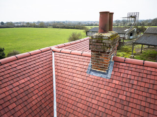 Inspection drone view of a newly installed ceramic roof on an old English farmhouse. The old, brick built chimney stack is visible. © Nick Beer