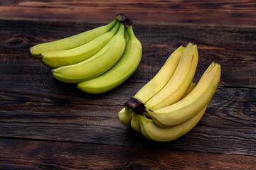 Green, yellow bananas arranged in row on wooden table. ripe and unripe banana
