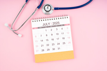 July 2025 desk calendar and Medical stethoscope on  pink background.