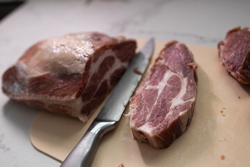Closeup of a pork shoulder cut being sliced, showcasing its marbled texture on a wooden cutting board