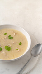 Close-up of Georgian traditional chicken soup Chikhirtma in the white plate on the light beige background