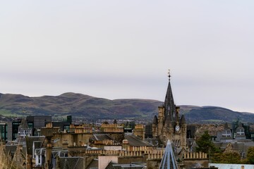 Fototapeta premium View of Edinburgh's historic skyline with the clock tower against rolling hills under a cloudy sky.
