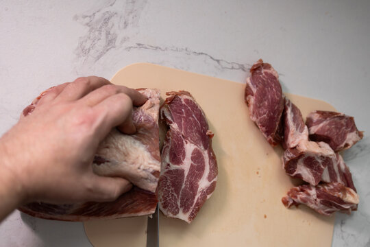 A skilled hand expertly slicing fresh pork meat on a robust wooden chopping board in a stylish modern kitchen - Powered by Adobe