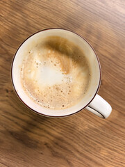 Cappuccino cup on wooden tabletop in coffee shop, top view.