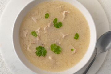 Georgian traditional chicken soup Chikhirtma in the white plate, flat lay on the light beige background