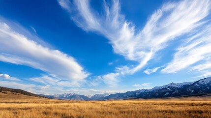 Fototapeta premium A breathtaking landscape of an open field under a blue sky with rocky mountains in the distance : Generative AI