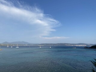 A panoramic seascape with sailboats floating on calm blue waters, framed by distant mountains. A dreamy travel destination