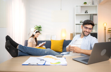 Portrait of a young freelancer smiling while working online via laptop at home with his girlfriend