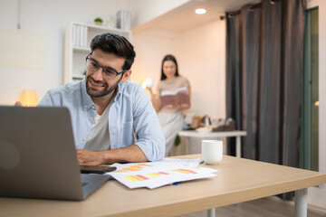 Portrait of a young freelancer smiling while working online via laptop at home with his girlfriend