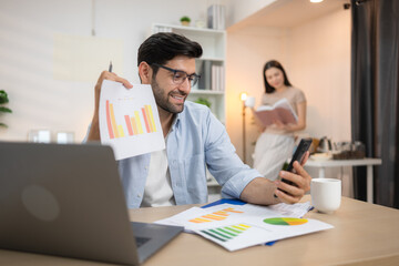 Portrait of a young freelancer smiling while working online via laptop at home with his girlfriend