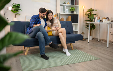 Obraz premium Young couple are smiling while relax and working online via laptop in living room at home