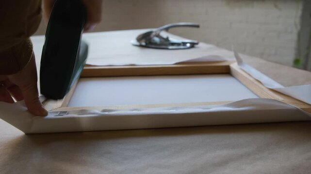 Hands stretching blank white canvas onto wooden stretcher. 