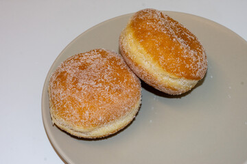 Two soft, golden donuts coated in sugar rest on a simple plate. Their fluffy texture and sweet aroma make them a delightful treat for any time of day