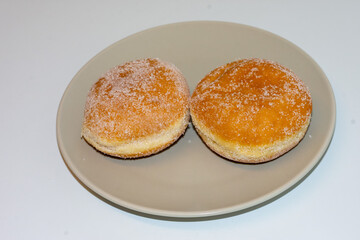 Two fluffy donuts with a golden crust covered in sugar are placed on a beige plate. Perfect for breakfast, dessert, or a sweet afternoon snack, they're invitingly fresh and soft