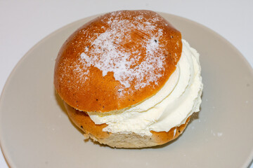 A delicious dessert sits on a plate, featuring a soft bun filled with generous whipped cream and lightly dusted with powdered sugar. This treat is perfect for afternoon enjoyment