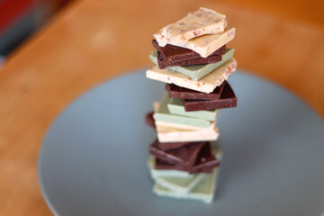 Pile of various chocolate pieces on a plate. Dark, white and matcha chocolate. Selective focus.