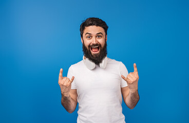 A cheerful bearded man wearing white headphones expresses joy with rock hand gestures. The vivid...