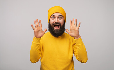 A cheerful man with a beard in a yellow beanie and sweater showing excitement. His expression and...
