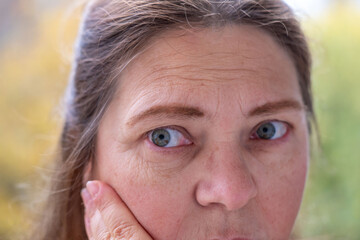 woman 50-55 years old seen deep in thought while looking herself in mirror, mature female face,...