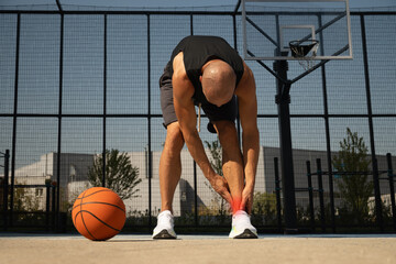 Naklejka premium Basketball ankle injury or pain. Basketball player check legs after workout of sport stadium. Professional athlete or sportsman with accident. Man check pain in leg after sport workout.