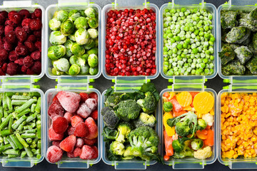 Plastic containers with frozen vegetables. Top view. On a gray stone background. Winter supplies of food.
