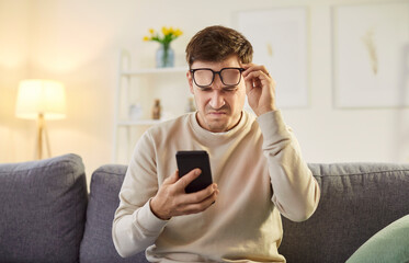 Young man wearing eyeglasses trying to read message on his smartphone having farsightedness eye...