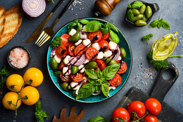 Fresh summer salad: tomatoes, mozzarella cheese, basil and olives. Caprese. On a gray concrete background.