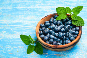 Blueberries in a wooden bowl. Top view, on a blue wooden background. Berries close-up.