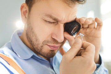 Close up of skilled jeweler closely inspecting gemstone in ring with magnifying glass. Expert...