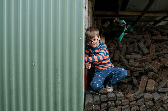 Young Boy Playing and Hiding in Pile of Peat Bricks at Home