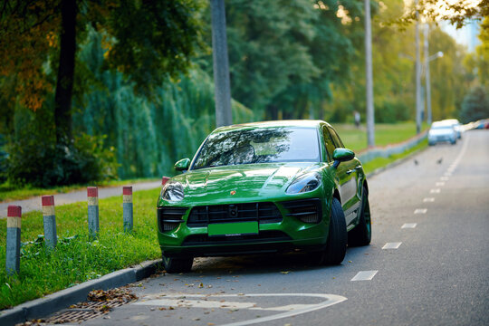 Minsk, Belarus. Aug 20, 2024. Green Porsche Macan GTS parked by the roadside near city park against backdrop of green trees. SUV with elegant design, modern curves, and high-end German engineering