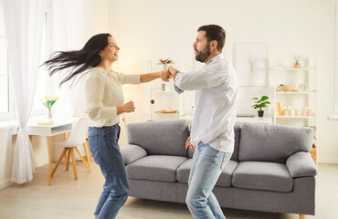 Fototapeta premium Two people dancing at home. Happy married couple having fun together. Young man and woman in casual clothes dancing in the living room. Family, love, romance, fun, leisure concept